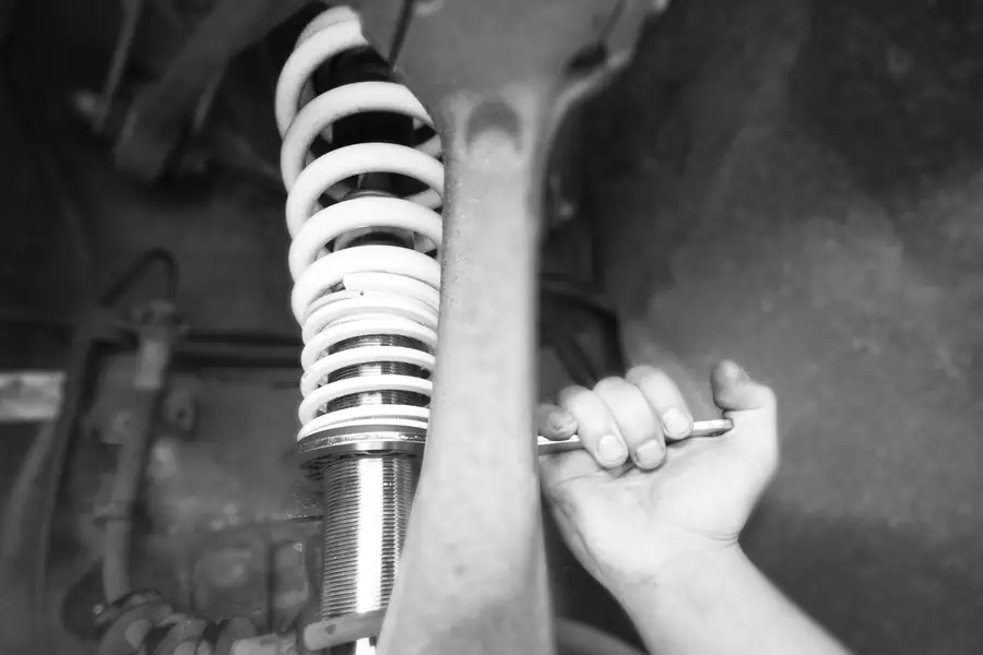 Schwarz-Weiß-Detail: Eine Hand zieht mit dem Schraubenschlüssel ein Gewindefahrwerk nach.