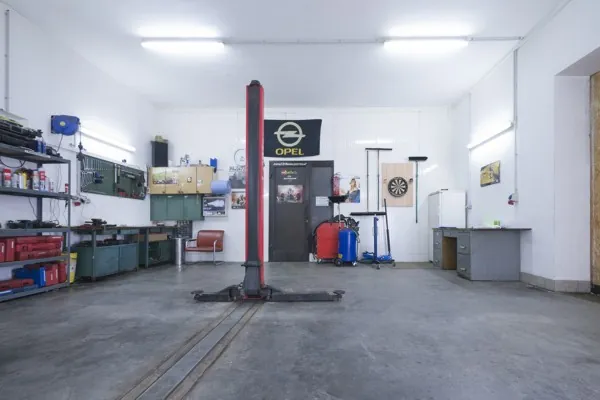 Werkstatthalle mit Hebebühne, Regalen und einer Opel-Fahne an der Rückwand.